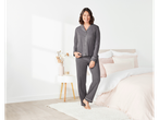 A woman smiles while wearing a gray pajama set in a bedroom setting.