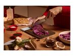 Person chopping red cabbage on a wooden board, surrounded by spices and bread.