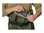 Man in green waders putting a fishing tackle box into a pocket.