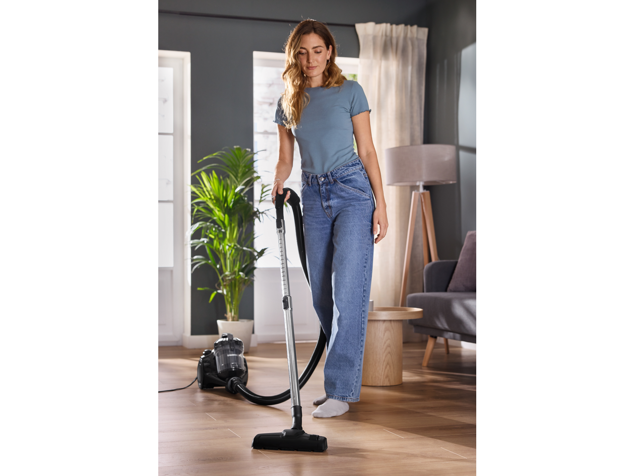 Mulher a aspirar um chão de madeira com um aspirador sem saco numa sala moderna.