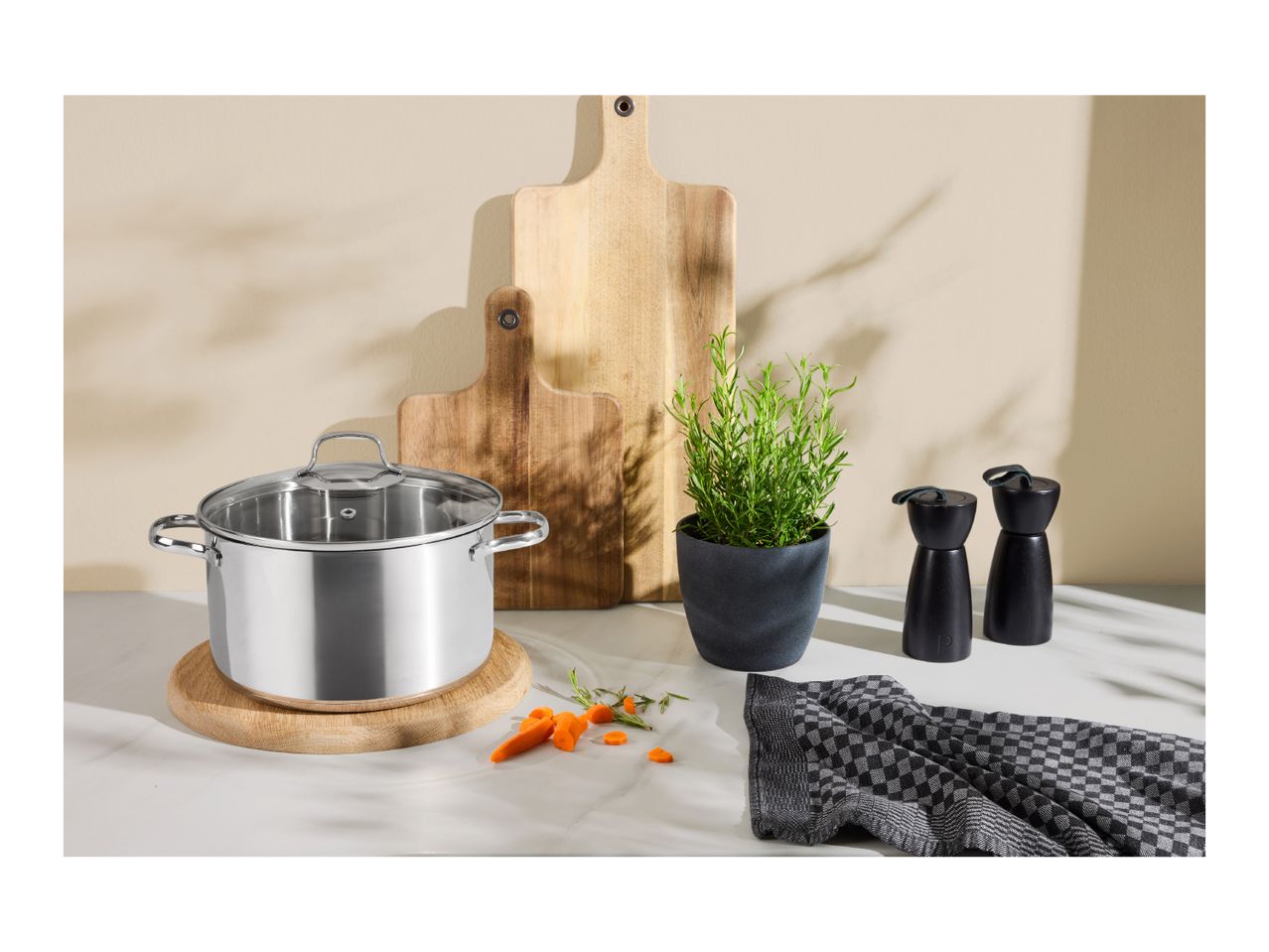 Stainless steel pot on a wooden trivet, with cutting boards, rosemary, and pepper grinders.