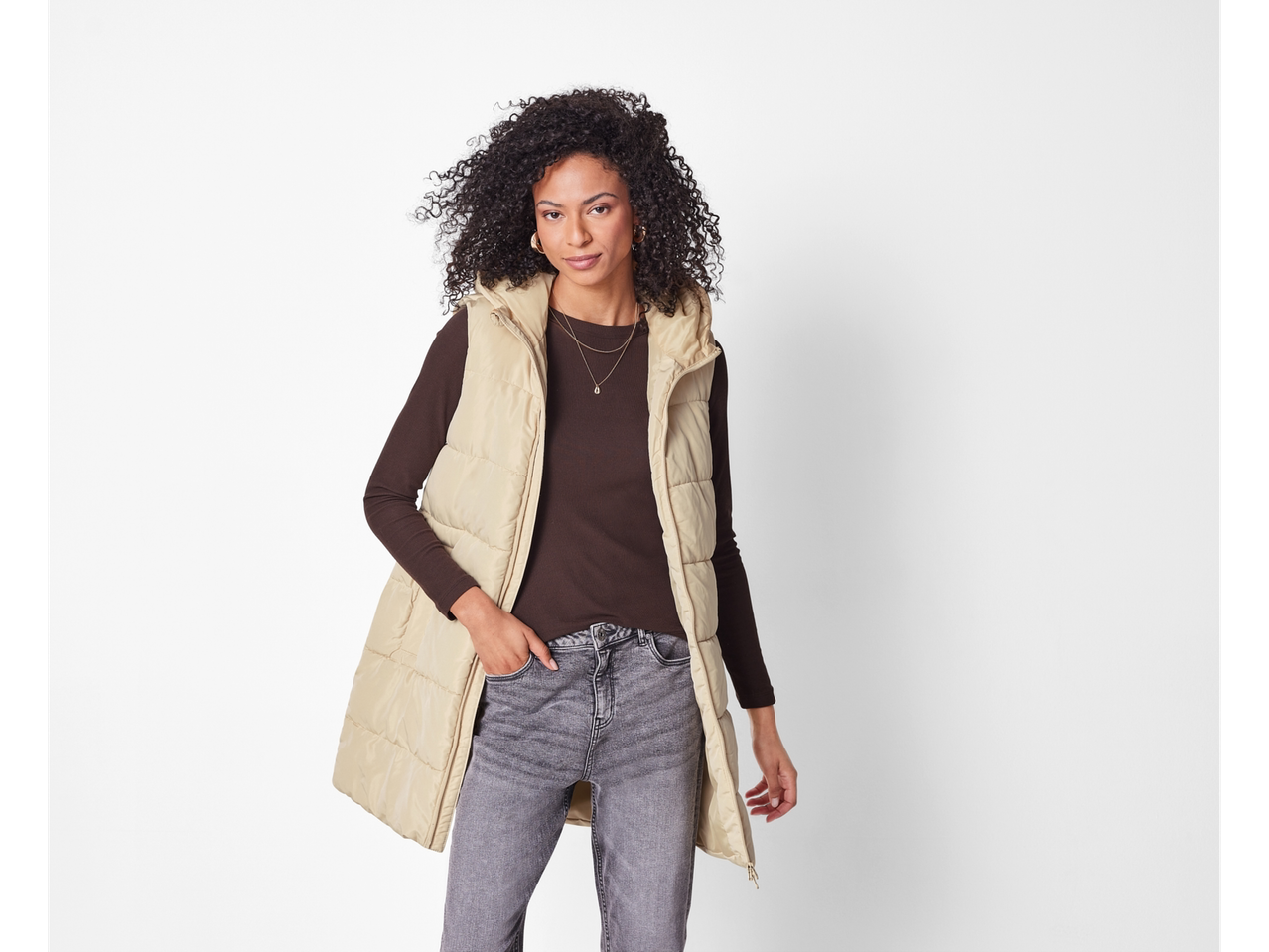 Donna che indossa un gilet lungo beige esmara® sopra una blusa marrone e jeans grigi.