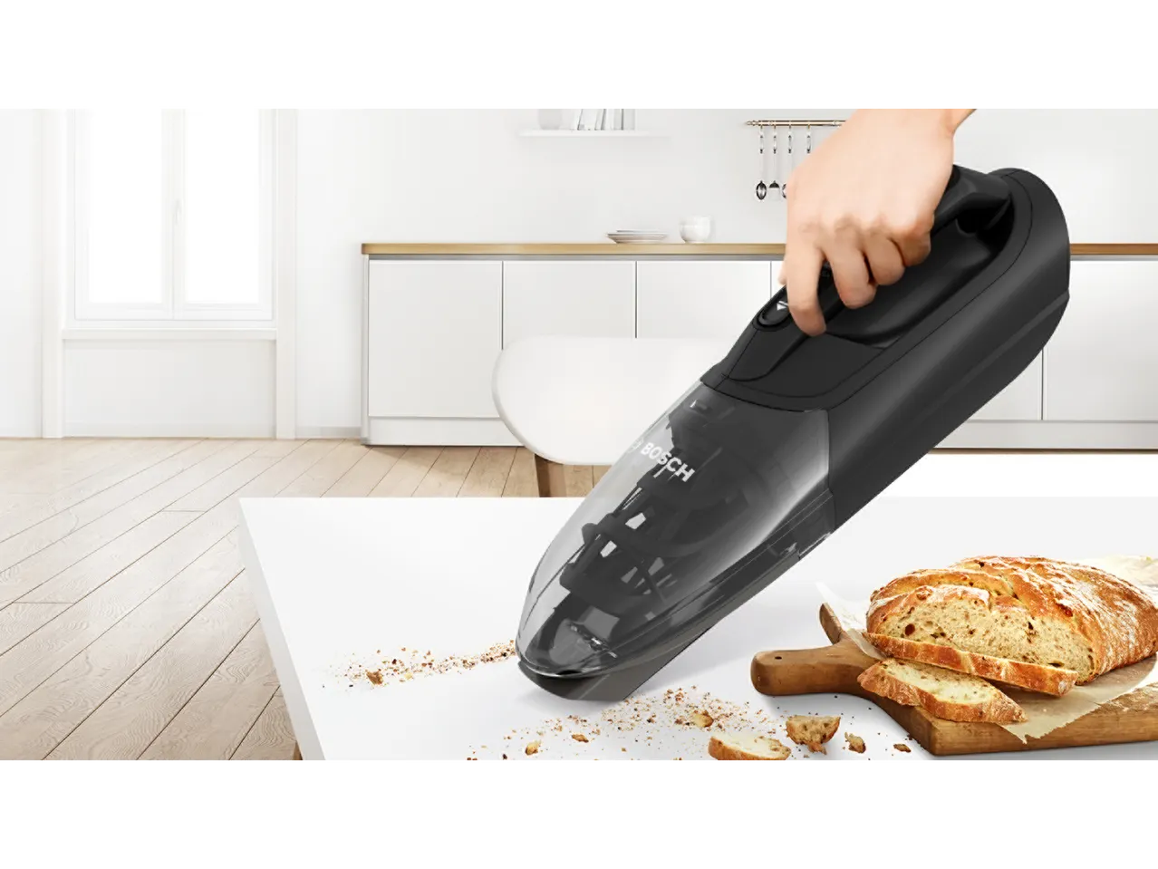 Aspirator de mână care adună firimituri de pâine de pe un blat alb de bucătărie.