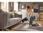 Mulher a aspirar debaixo do sofá com o aspirador vertical sem fios 2 em 1 Silvercrest®.