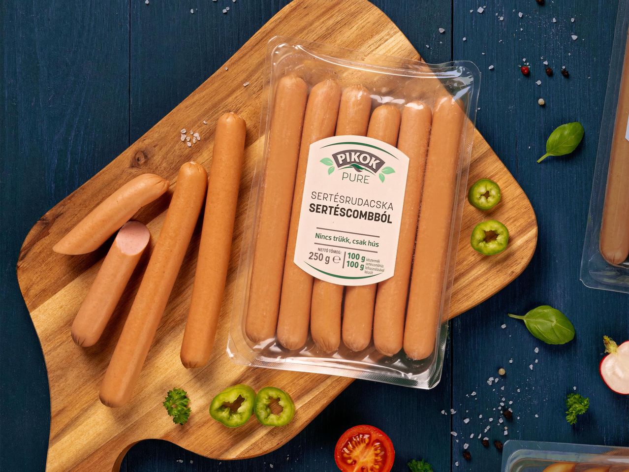 Sertésrudacskák csomagolásban és vágódeszkán, zöldségekkel és fűszerekkel.