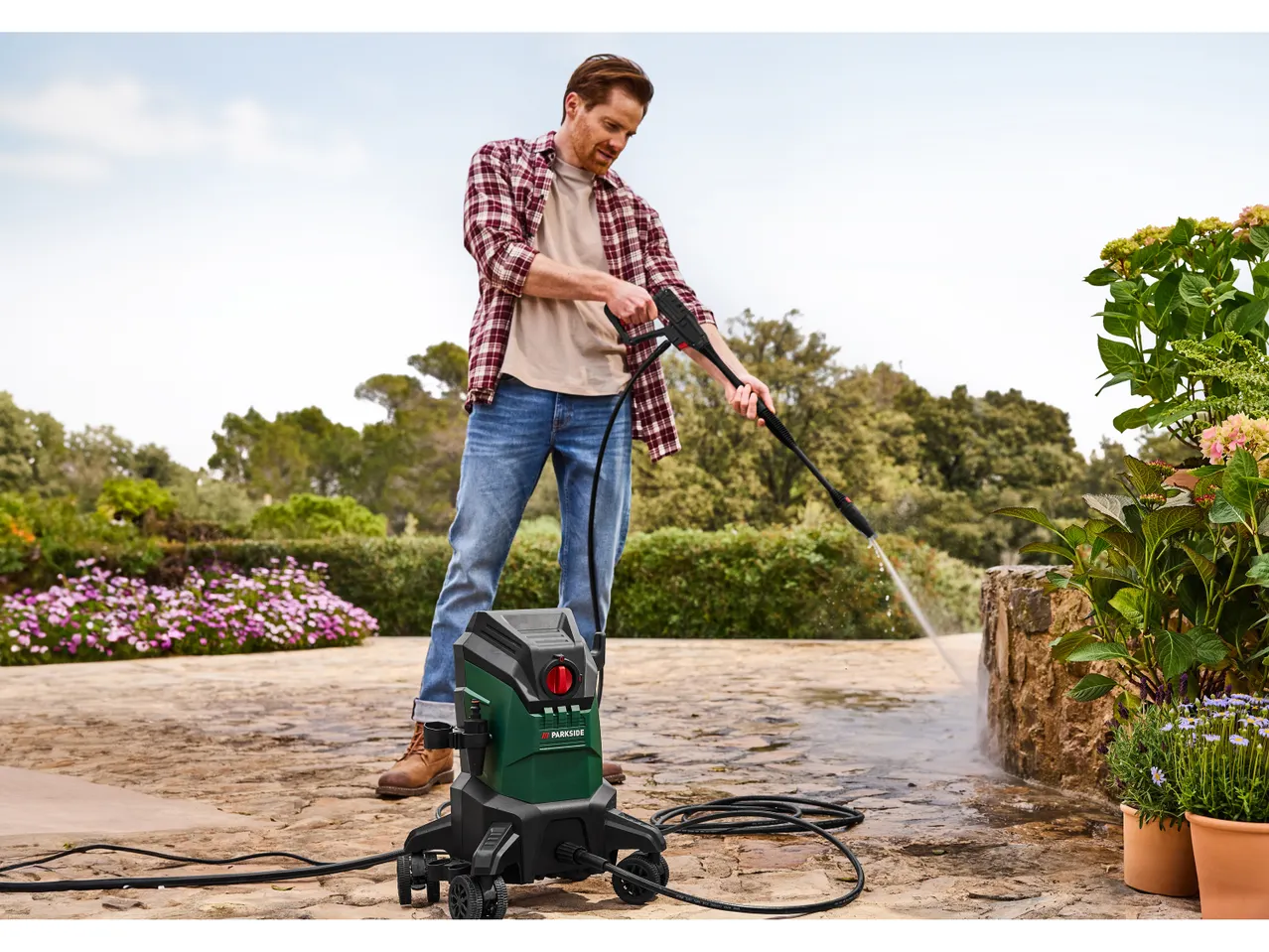 A man uses a PARKSIDE® Flexi Pressure Washer to clean a patio.