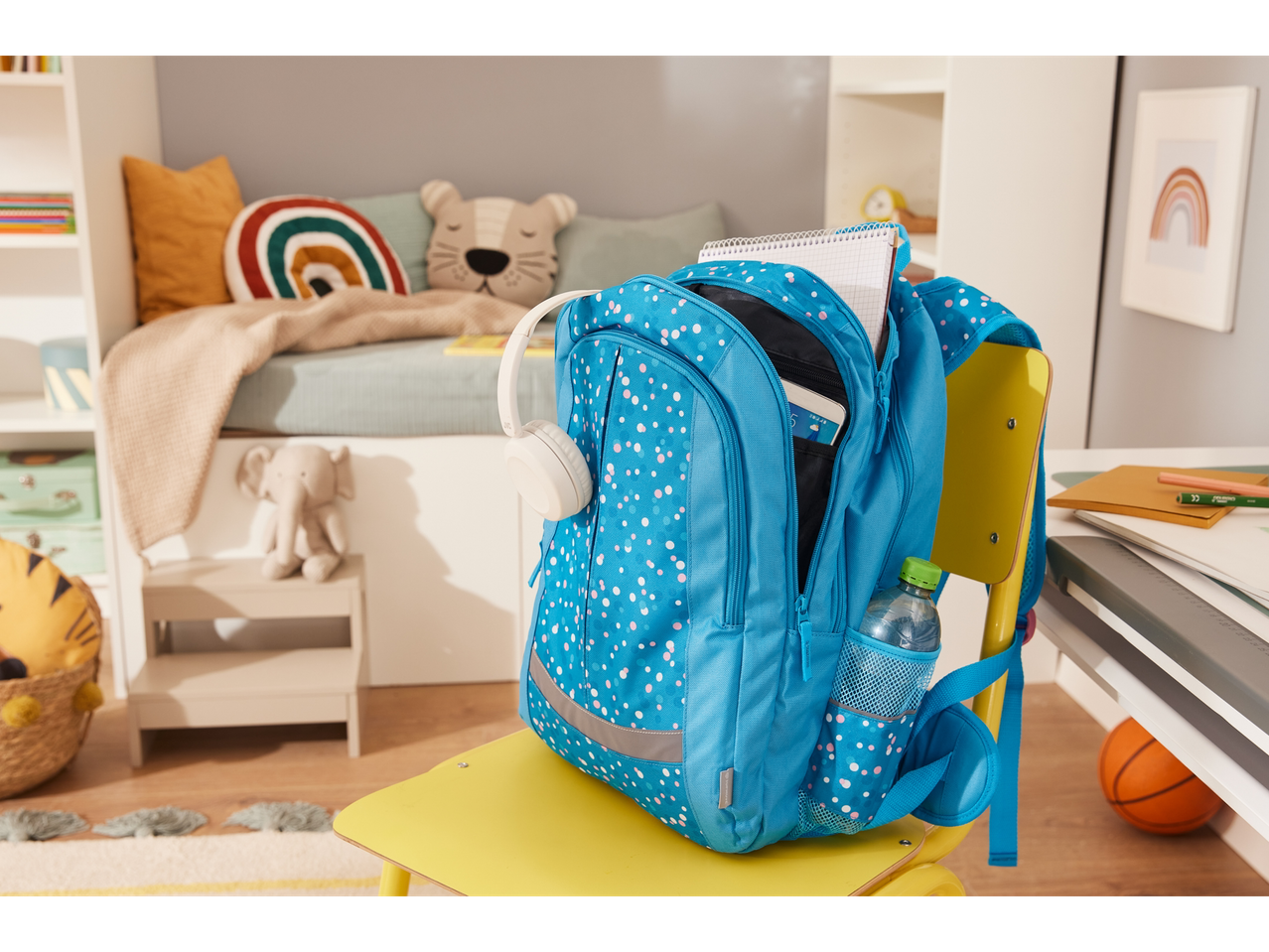 Uma mochila azul com bolinhas está em uma cadeira amarela em um quarto infantil.
