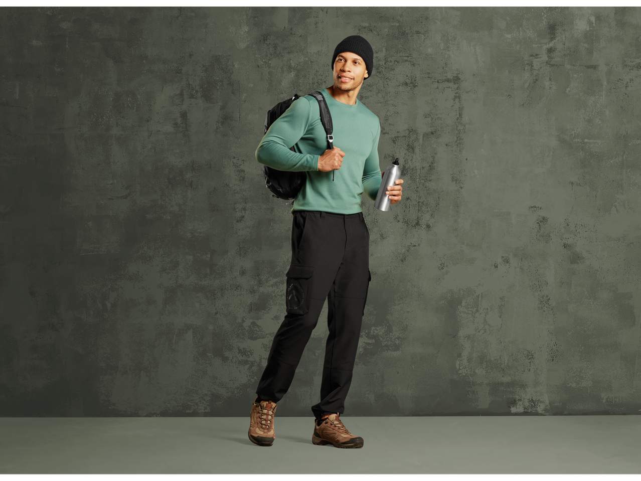 Man in CRIVIT thermal sports trousers, green long-sleeve shirt, and beanie, holding a water bottle.