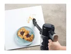 Handheld vacuum cleaner cleaning crumbs from a white table next to pastries on a plate.