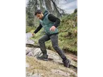 Man in a teal thermal sports gilet and dark pants hiking on a rocky trail.