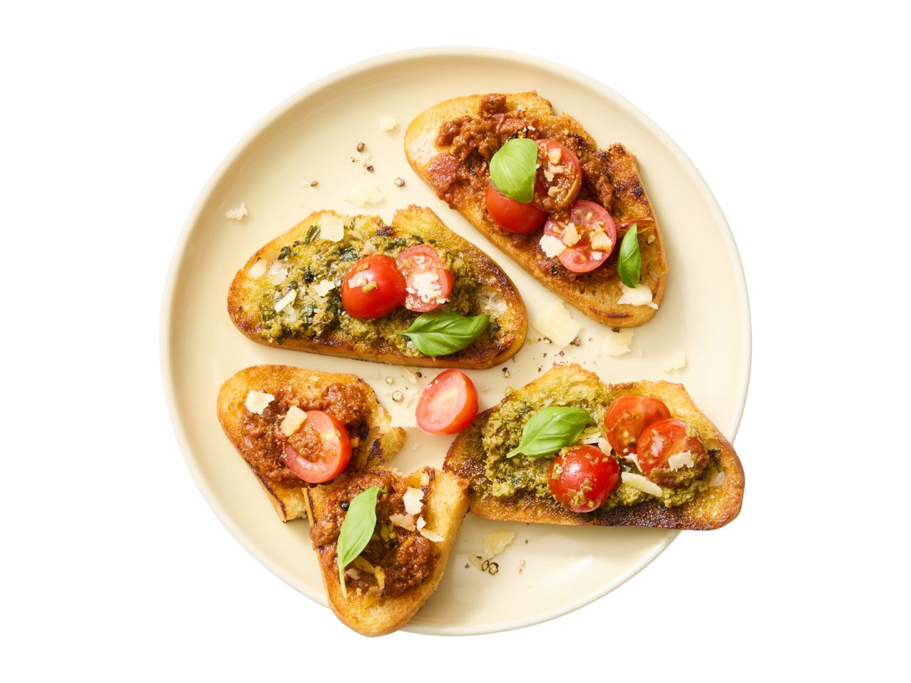 A plate of bruschetta with pesto and tomato tapenade, garnished with cherry tomatoes, basil, and cheese.