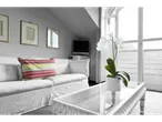 Um sofá branco com uma almofada listrada e uma mesa de centro de vidro branco com uma orquídea branca.
