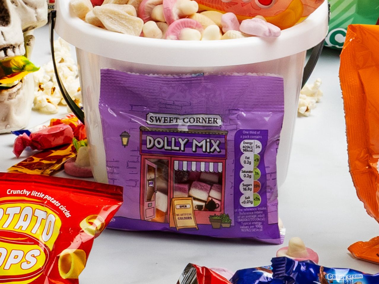 A bucket of Dolly Mix candy, a bag of potato circles, and other sweets for Halloween.