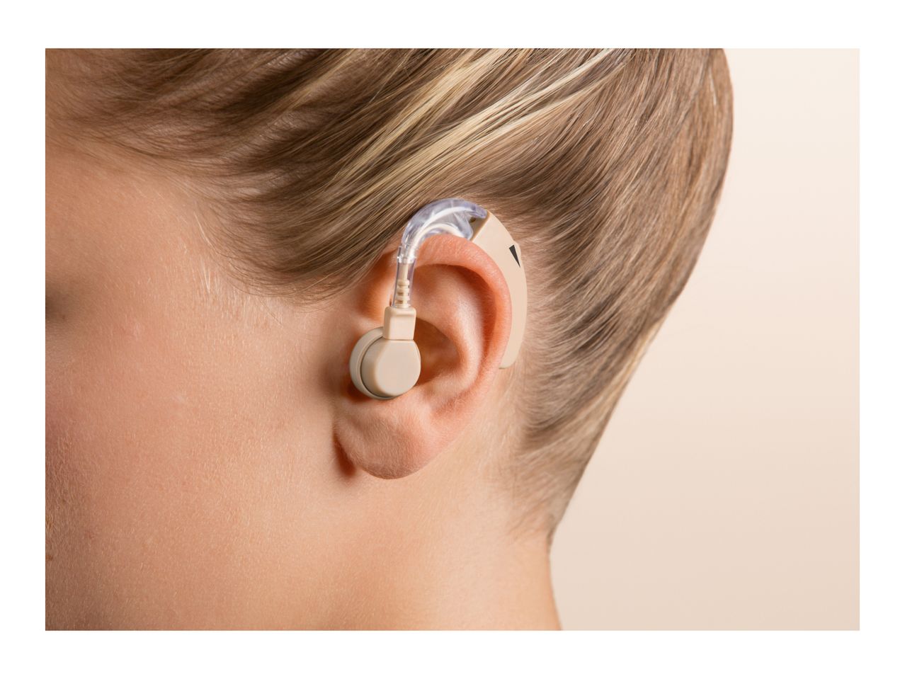 Close-up of a person's ear with a beige hearing aid, showing the device clearly.