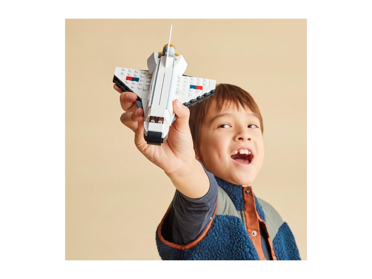 A boy holding a white toy space shuttle, smiling with his mouth open.