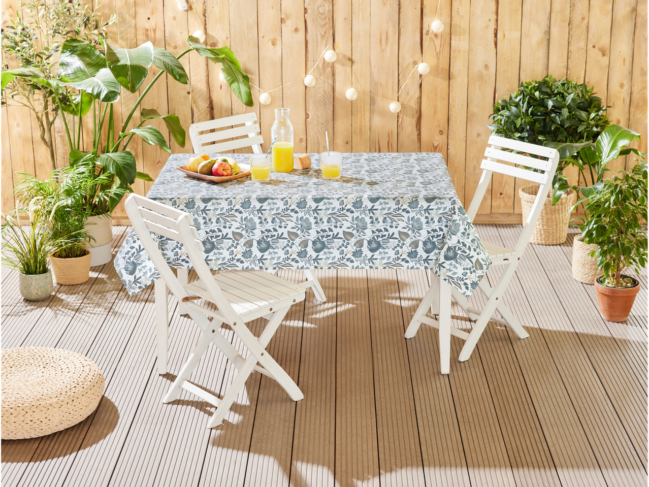 Garden table with floral tablecloth, white folding chairs, and green plants.