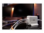 White multi-port charging station with several cables plugged in, on a desk with monitors.