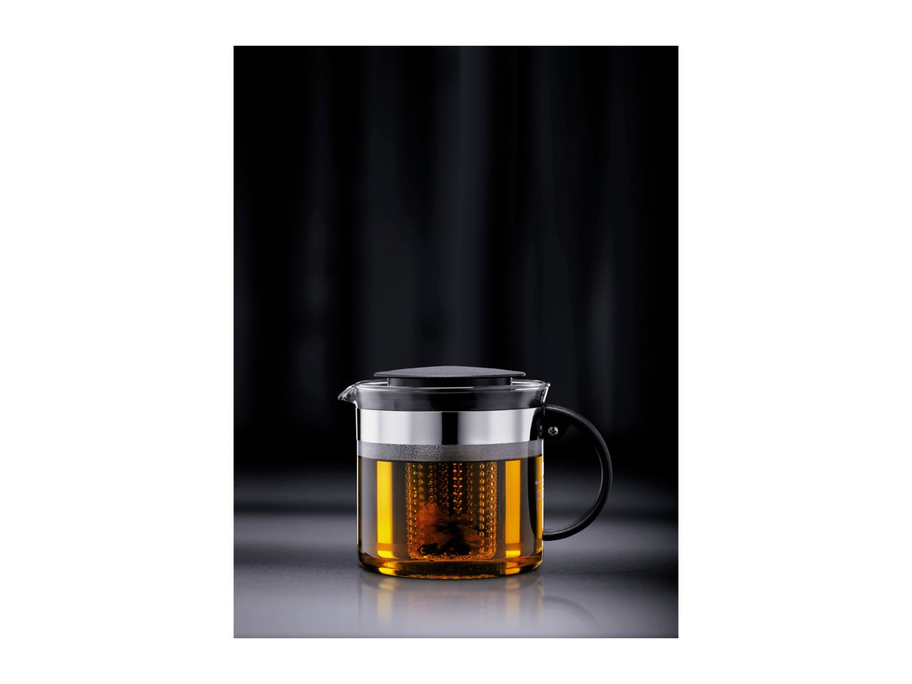 Glass teapot with a black lid and handle, filled with amber tea and an infuser.
