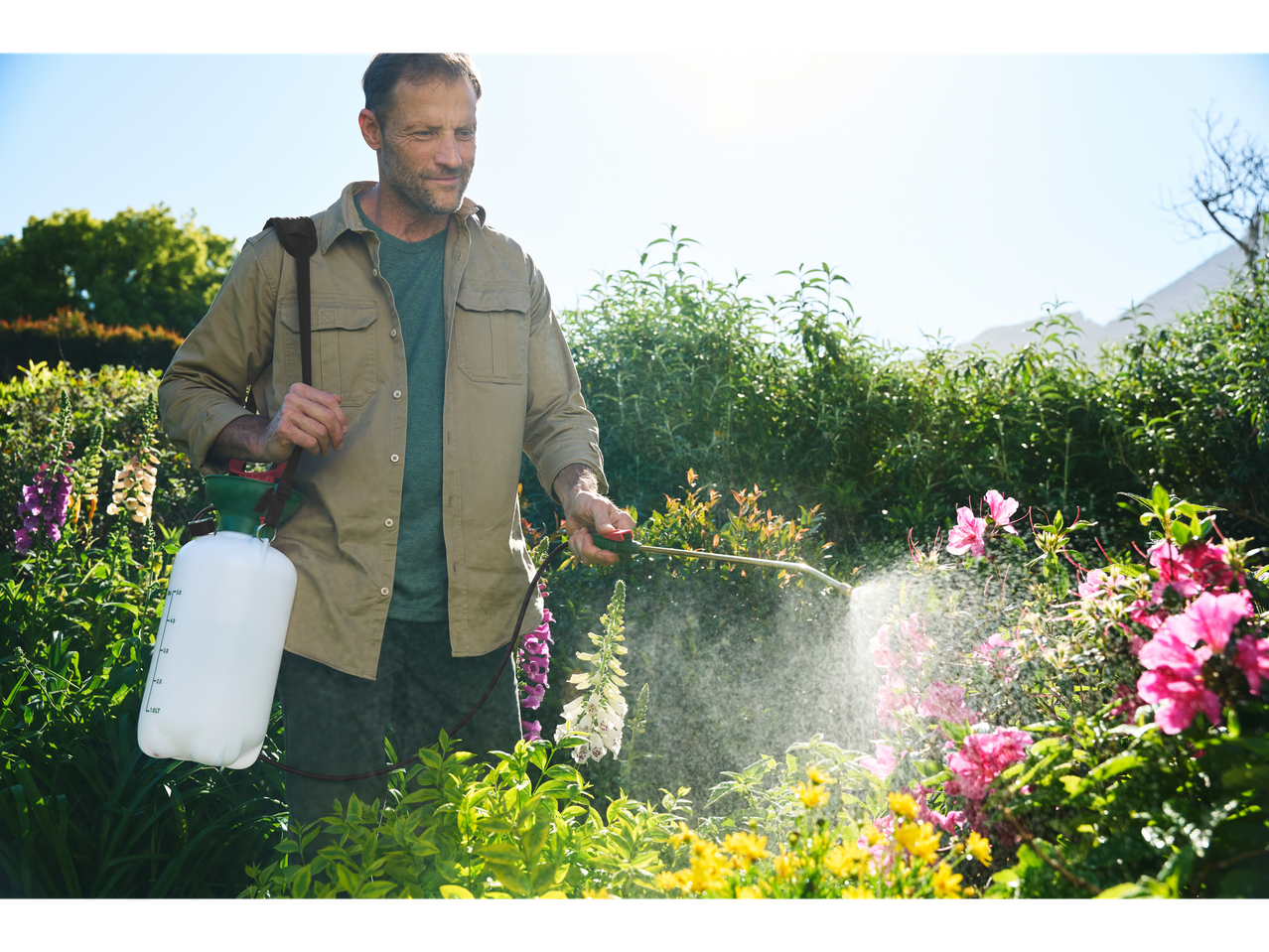 Man using a Parkside® garden sprayer to water plants in a sunny garden.