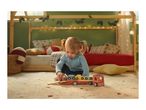 Toddler playing with a wooden car transporter toy on a rug in a festive bedroom.