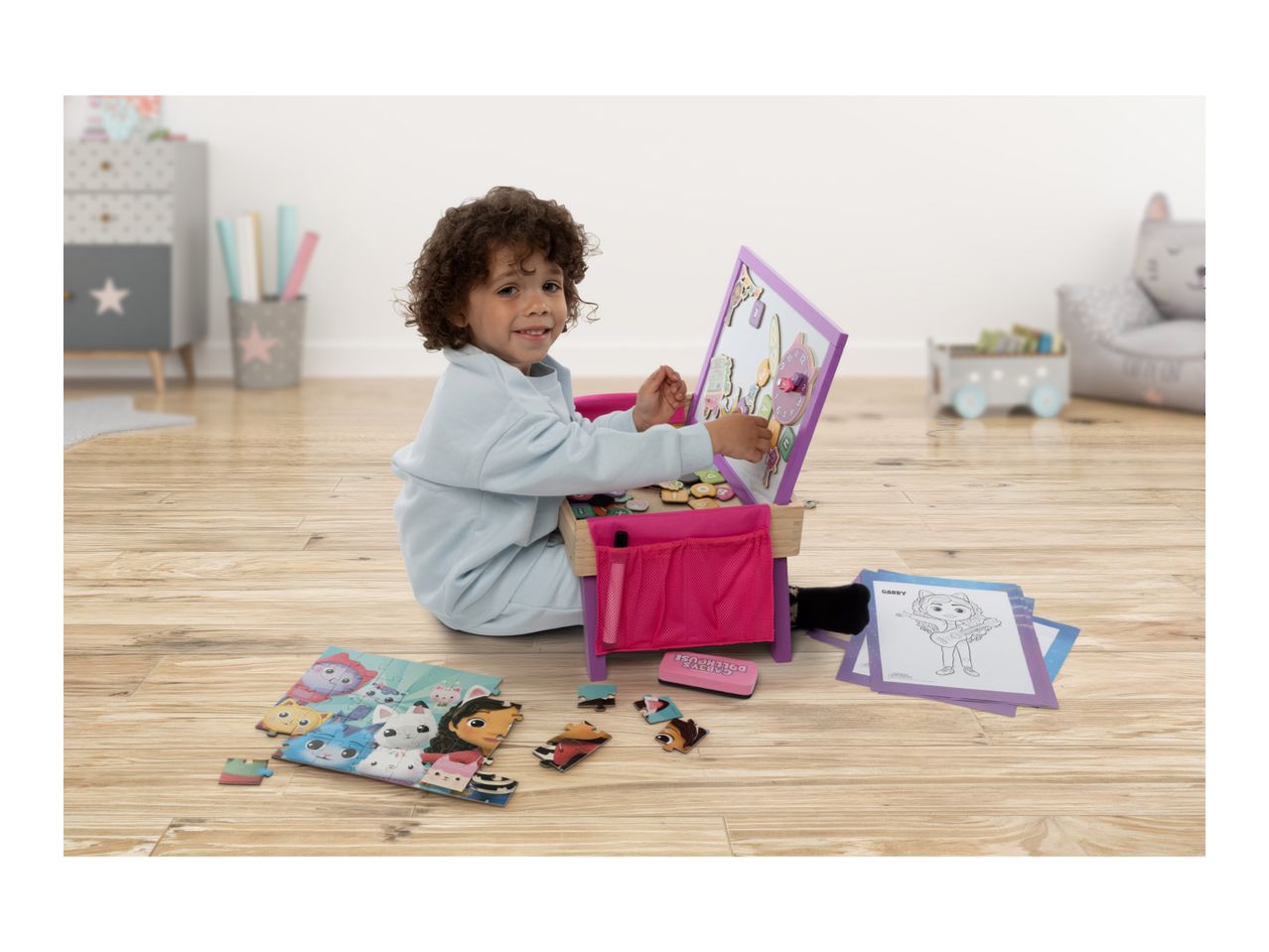 A child playing with a magnetic easel and puzzle on a wooden floor.
