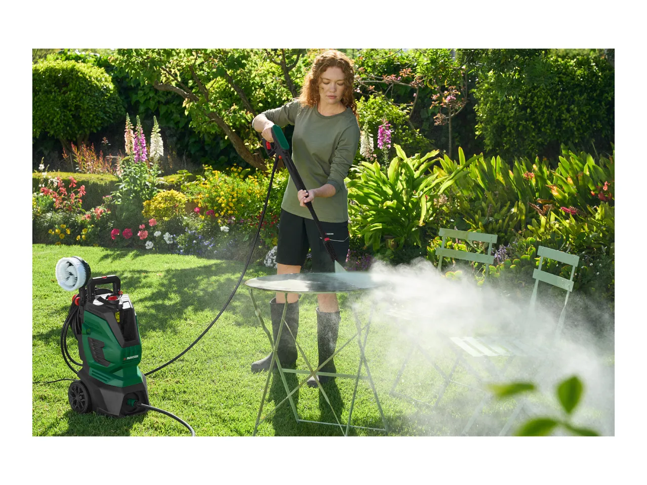 Woman pressure washing a garden table with a pressure washer in a lush garden.