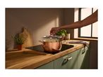 A person lifting the lid of a copper pot cooking on an induction hob