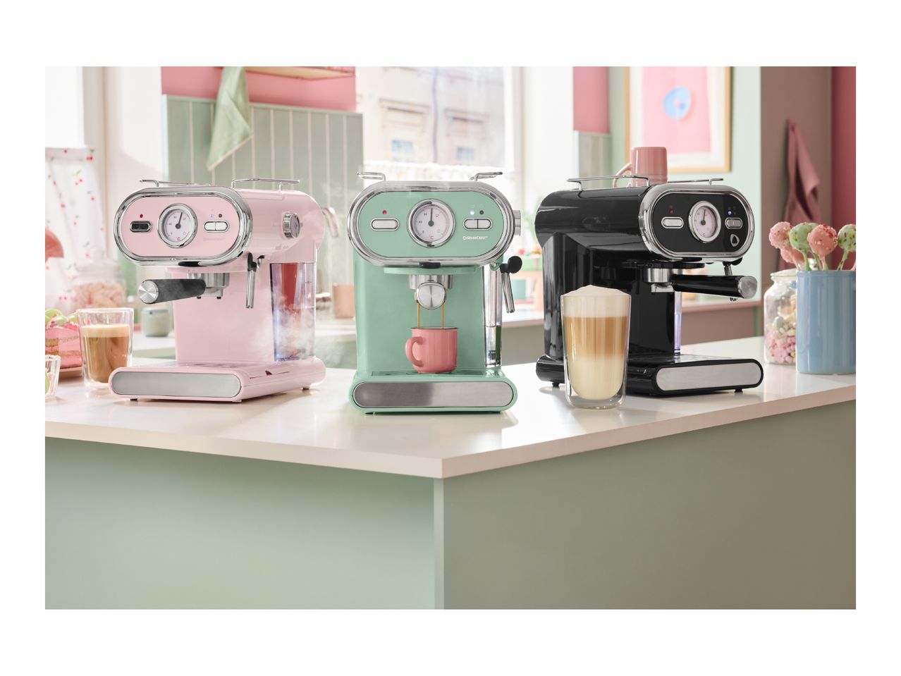 Three retro-style SilverCrest espresso machines in pink, mint green, and black on a kitchen counter.