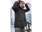 Man in a dark jacket and grey pants, adjusting his hood outdoors.