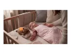 Baby in a pink sleep sack in a crib with a glowing plush toy.