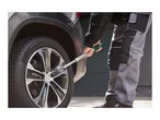 A person using an extendable wheel wrench to loosen a lug nut on a car wheel.