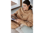 A woman in a tan hoodie and sweatpants reading a magazine on a couch.