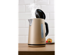A beige Silvercrest electric kettle with steam rising, next to a pastry on a wooden counter.