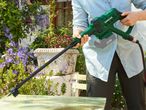 A person uses a Bosch pressure washer to clean a patio table.