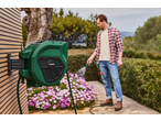 A man watering pink flowers with a green hose reel mounted on a wooden wall.