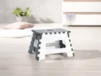 Sgabello pieghevole bianco e grigio con puntini, su pavimento di legno chiaro.