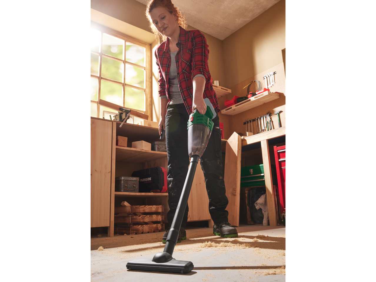Woman using a PARKSIDE® 20V Cordless Handheld Vacuum Cleaner to clean sawdust.