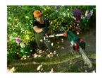 Man in protective gear using a pole chainsaw to cut a tree branch, with wood chips flying.