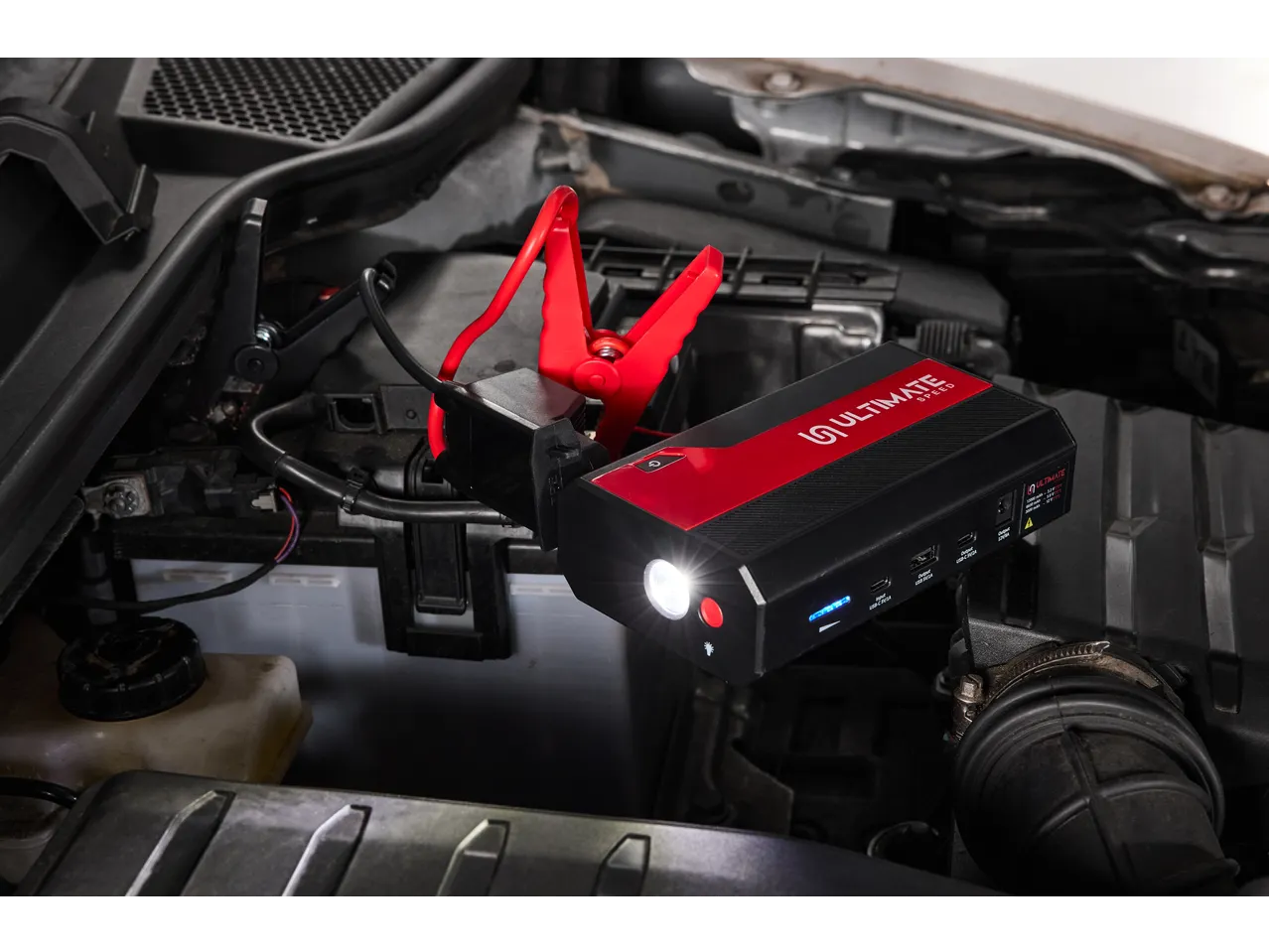 Arrancador portátil com pinças conectadas a uma bateria de carro no compartimento do motor.