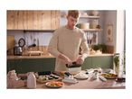Man making sushi with a sushi maker, rice, salmon, and vegetables on a wooden table.