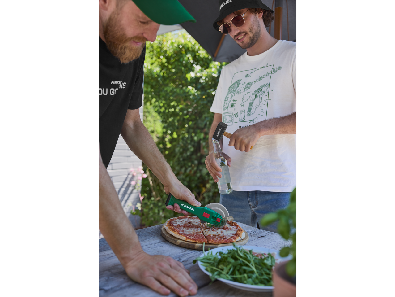 Homens dividindo pizza ao ar livre com um cortador de pizza Parkside.
