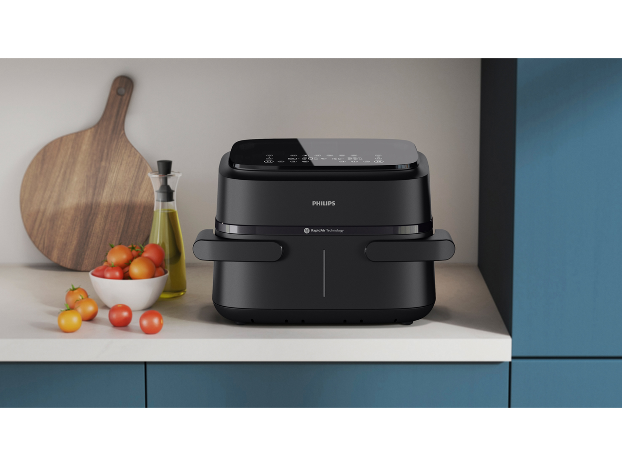 Black air fryer on a kitchen counter with tomatoes and olive oil.