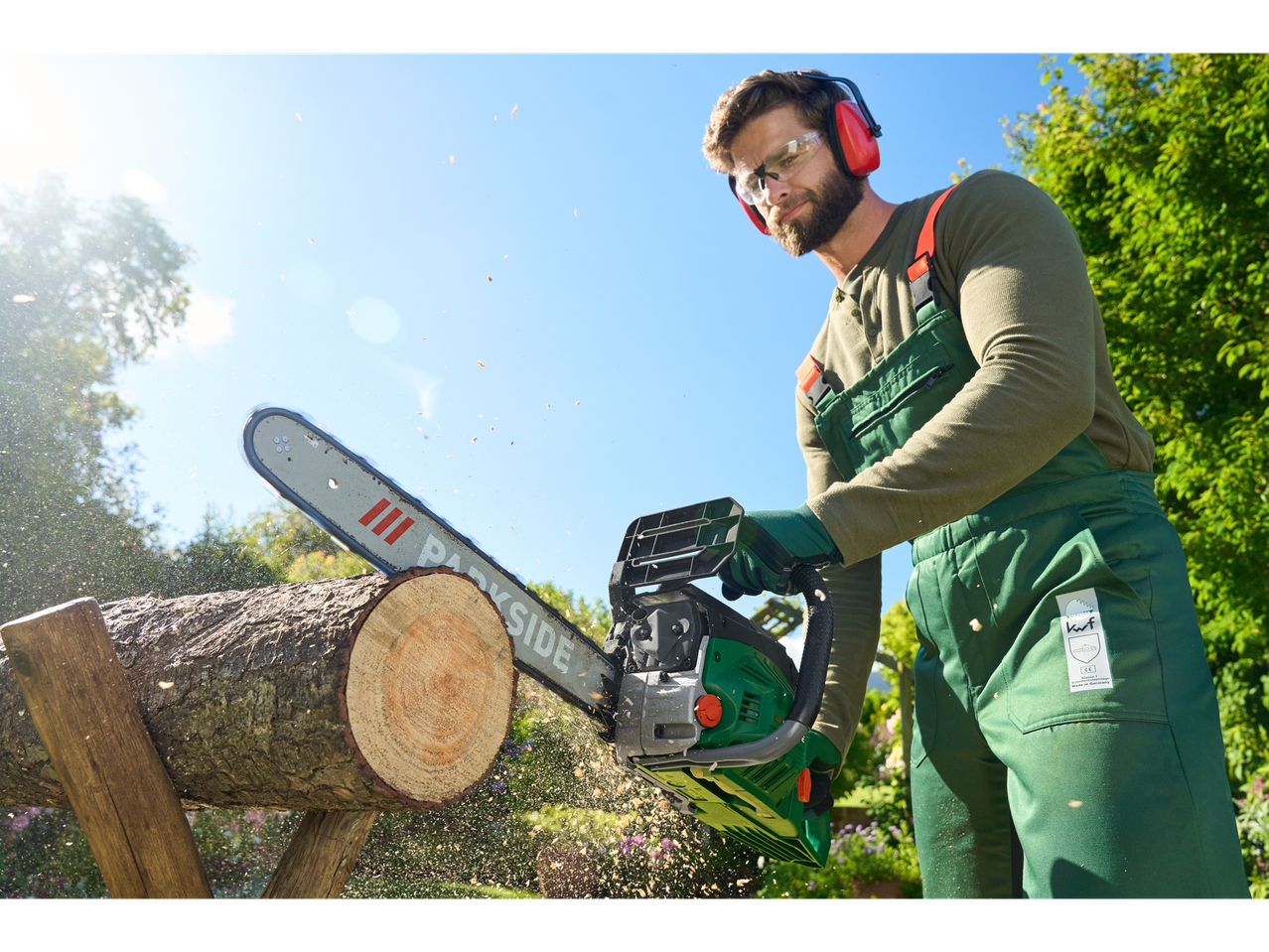 A man uses a Parkside chainsaw to cut a log outdoors.