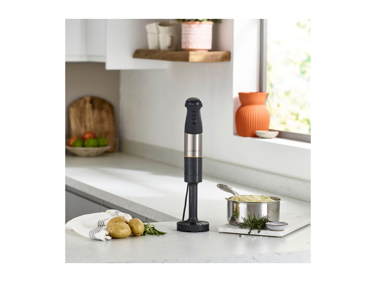 Hand blender on a kitchen counter with potatoes and mashed potatoes in a pot.