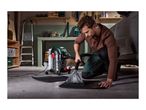 A man cleaning a car mat with a wet and dry vacuum cleaner in a garage.