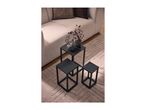 Three black nesting side tables of different heights on a beige rug next to a sofa.