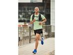 Un uomo sorridente corre indossando una maglietta verde, pantaloncini neri e scarpe da corsa blu.