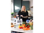 Woman in kitchen with Delonghi food processor, Farrells potatoes, Delacre pasta, and fresh produce.
