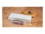 White vacuum sealer packaging a piece of meat on a wooden table next to herbs and garlic.
