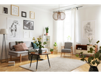 Sala de estar luminosa e moderna com sofá, poltrona, mesa de centro e quadros nas paredes.